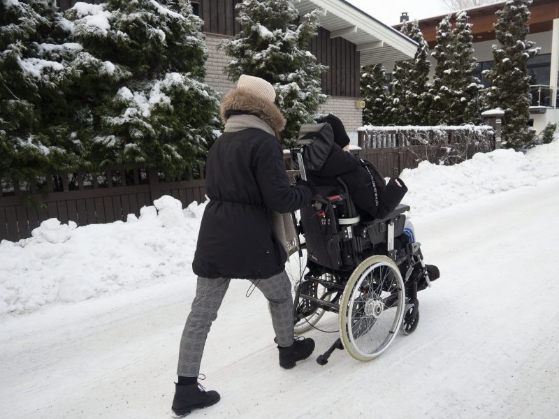 Kivioja työntää pyörätuolissa olevaa hoidettavaa jäistä mäkeä ylöspäin.