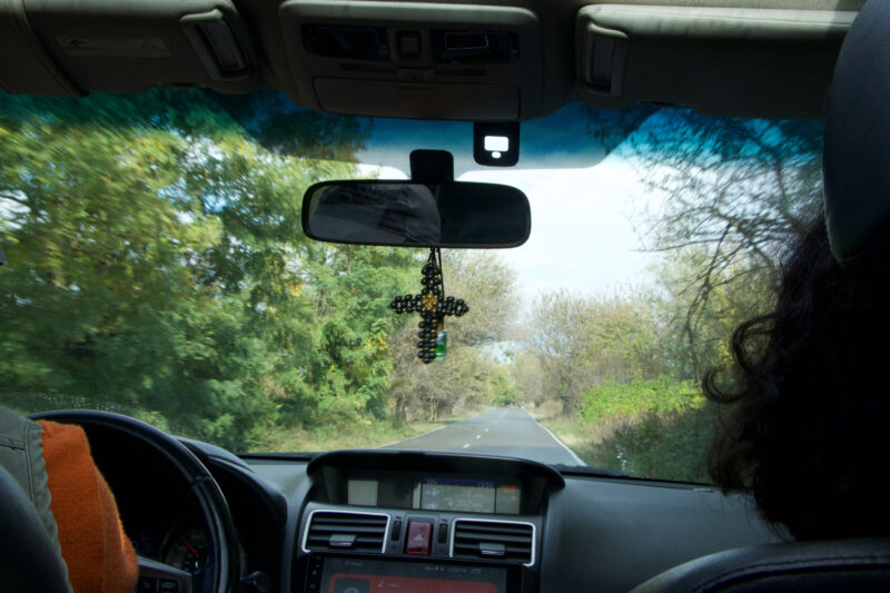 Auto ajaa pienen paikkakunnan hiljaisella tiellä Georgiassa. Etupeilistä roikkuu helmistä tehty risti, mikä on tyypillistä georgialaisissa autoissa.