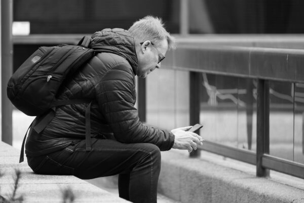 Keski-ikäinen miesoletettu henkilö selaa puhelintaan ja polttaa tupakkaa.
