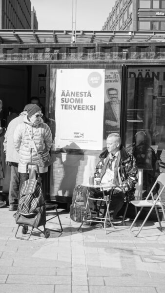 Mies istuu Perussuomalaisten vaalikontilla oluella.
