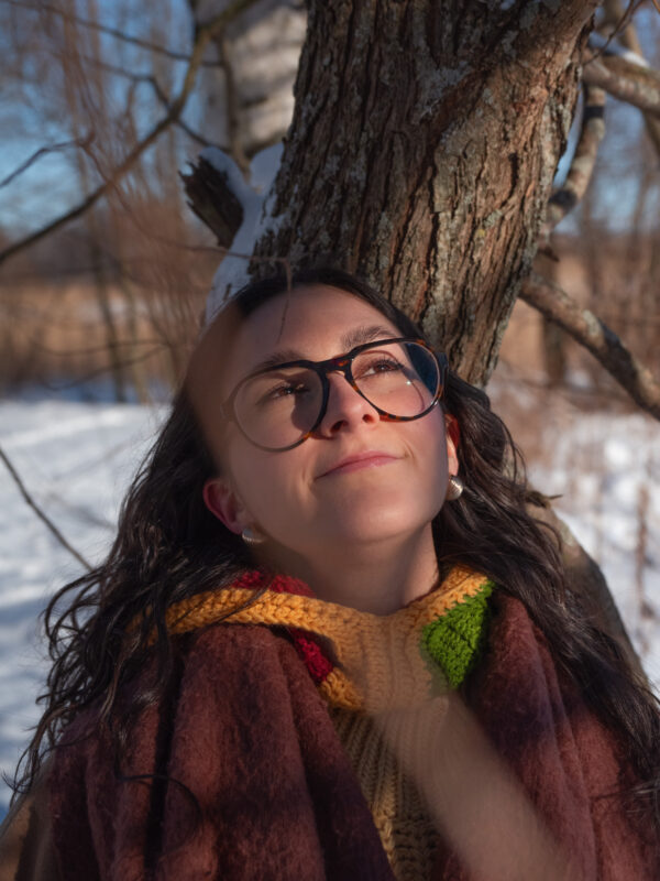 Auringon säteet laskeutuvat jazzlaulajan kasvoille oksien välistä hänen nojaillessa puuhun. Taustalla talvinen kaislikko.