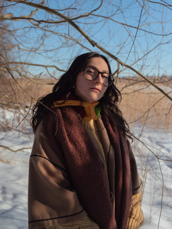 Auringon säteet laskeutuvat jazzlaulajan kasvoille puiden oksien läpi. Taustalla talvinen kaislikko.