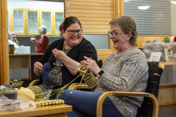 Kuvassa neulepiirin vetäjä ja jäsen keskustelevat nauraen.
